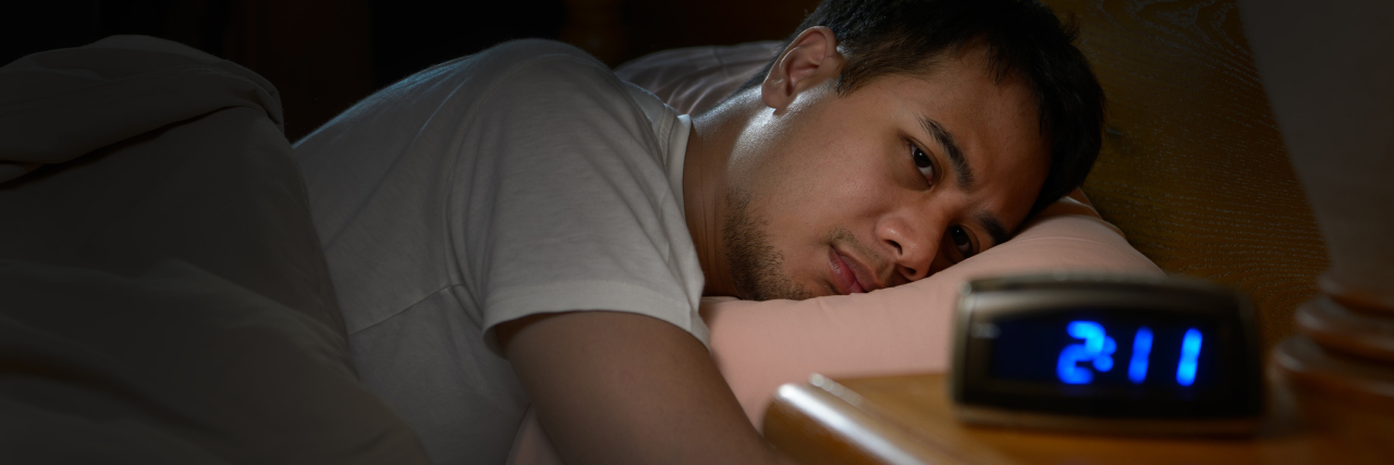 How to Prevent Chronic Insomnia man lying awake in bed staring at alarm clock that reads 2:11 AM