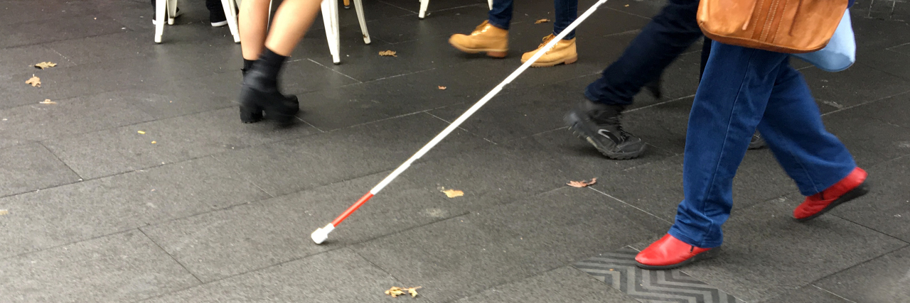 Visually impaired person walking down the street with a cane.