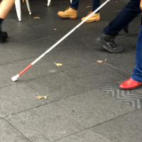Visually impaired person walking down the street with a cane.