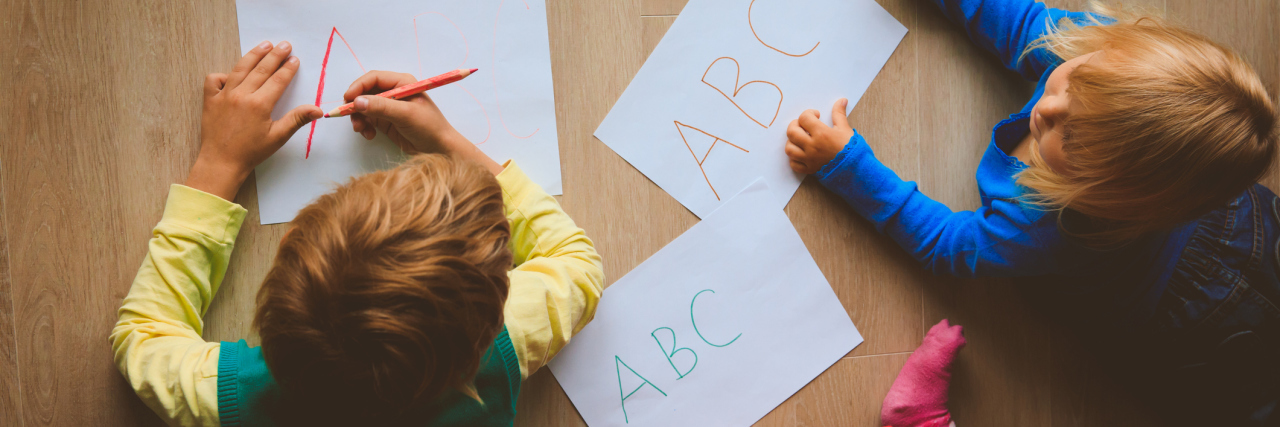 Three kids writing the ABC's on pieces of paper on the floor