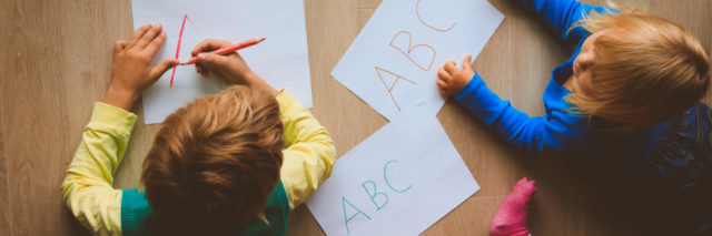 Three kids writing the ABC's on pieces of paper on the floor