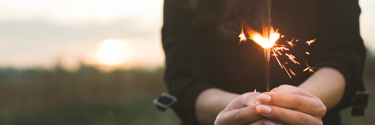 My New Year's Goals as a Woman With Chronic Illness woman wearing black shirt, standing in a field and holding a sparkler