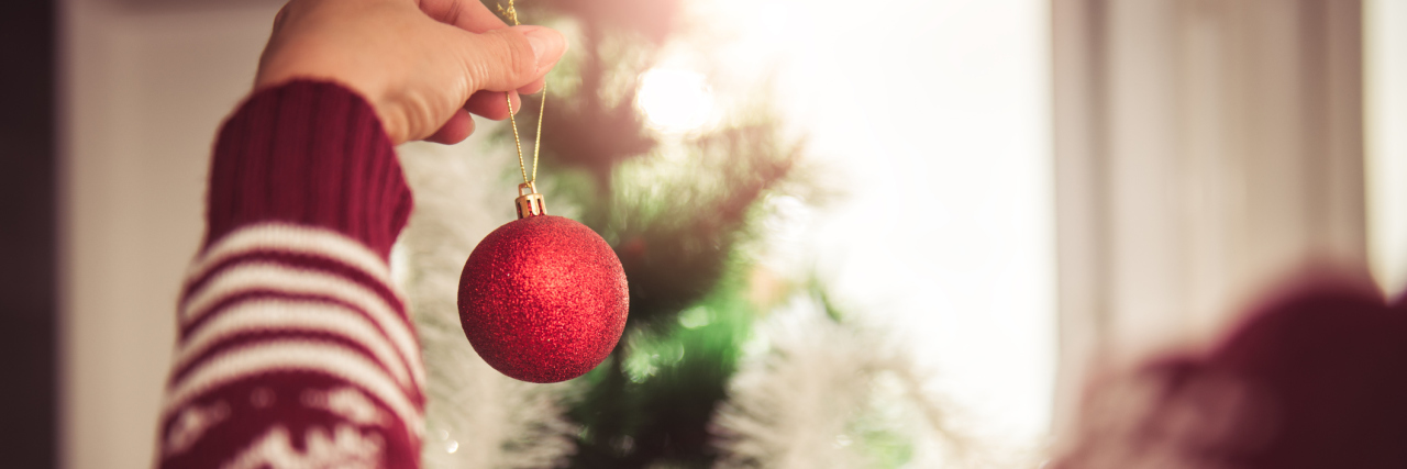 Tips for Navigating the Holidays With Thyroid Disease woman wearing red sweater and hanging a red ornament on the christmas tree