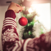 woman wearing red sweater and hanging a red ornament on the christmas tree
