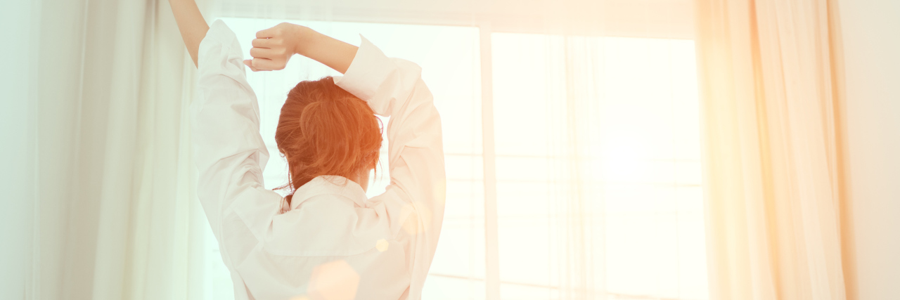 woman sitting on her bed and stretching her arms in the morning