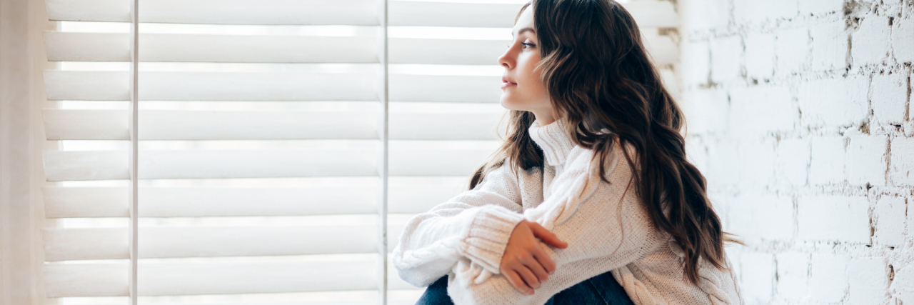 woman wearing a white sweater and sitting on a windowsill next to garland