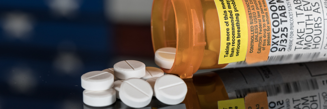 Oxycodone is the generic name for a range of opoid pain killing tablets. Prescription bottle for Oxycodone tablets and pills on wooden table with USA flag in background