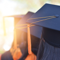 University graduates wearing a yellow tasseled cap, seen from the back.
