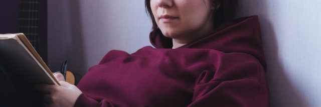 A young woman sitting in a bean back chair with a notebook in her hand. She's wearing a sweatshirt and looking at the viewer.