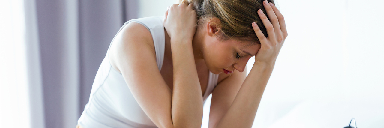 Tips for Living With an Anal Fistula A woman sitting on her bed, with her head in her hands.