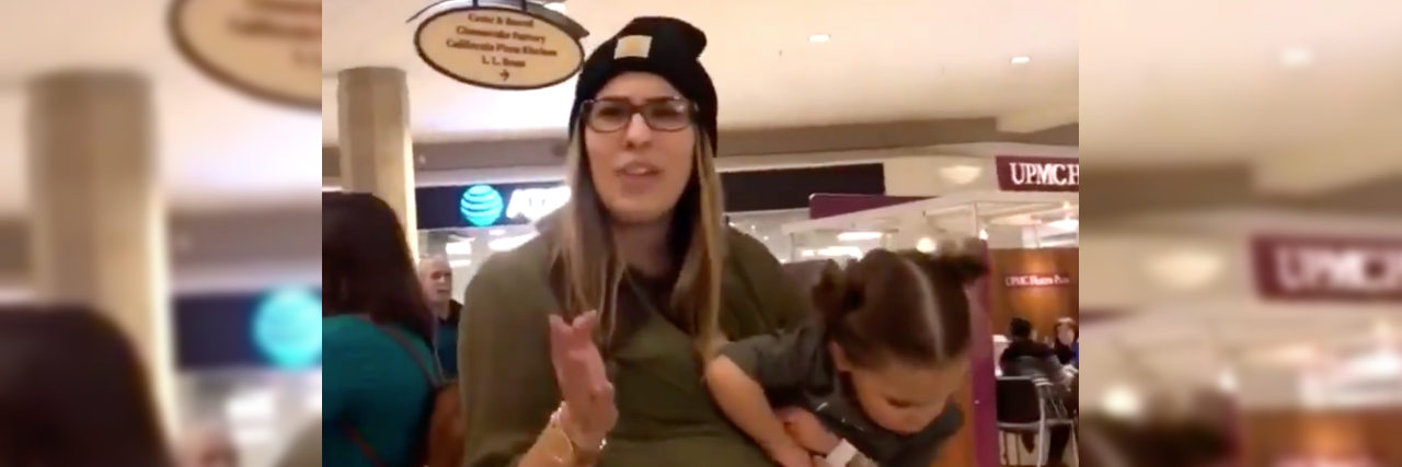 Mother Harasses Service Animals After Being Told She Couldn't Pet Them Mother holding her toddler daughter pointing at person filming. She's wearing a black beanie and a green blouse.