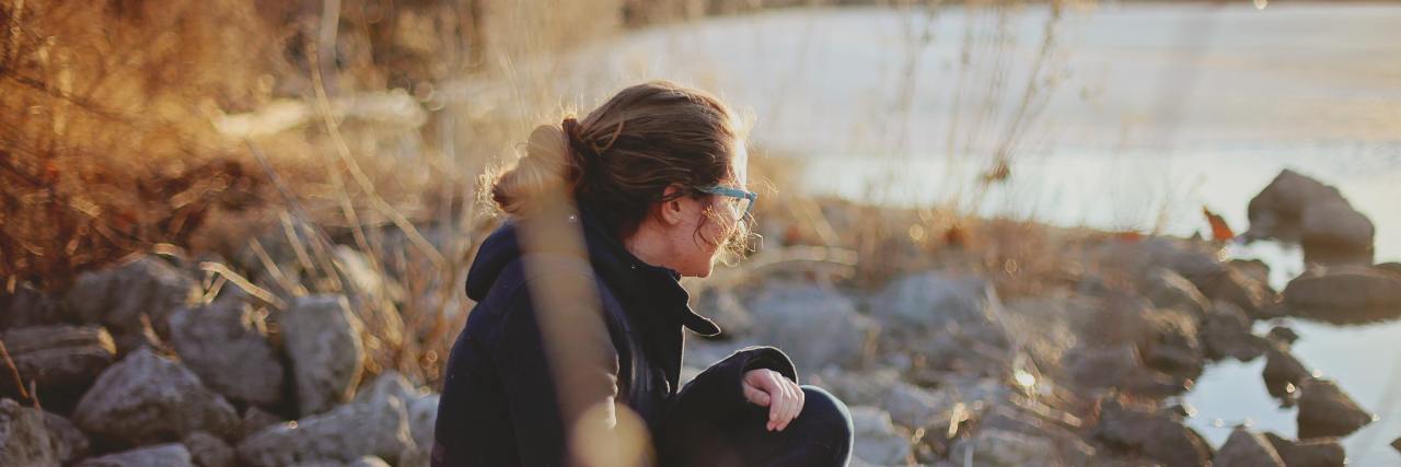 Should I Keep Asking Someone With Mental Illness to Do Things? woman sitting on beach rocks alone looking at water