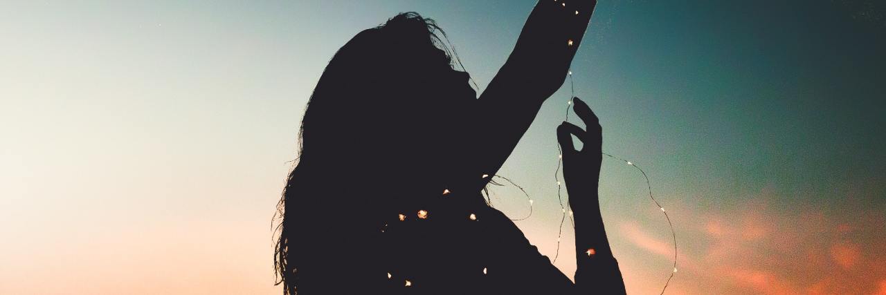 The Twenty One Pilots Lyric That Saved Me Life With Depression woman silhouetted by sunrise holding blurred fairy lights and hands raised to sky