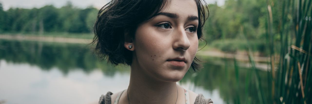 A (Bad) Day in the Life of Someone With Depression and Anxiety young woman with short hair looking depressed or anxious in front of lake and trees
