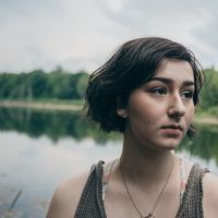 young woman with short hair looking depressed or anxious in front of lake and trees