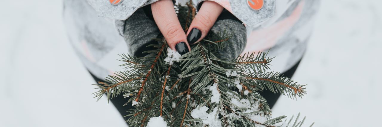 Holiday Self-Care Plan Advice for Mental Health close up photo of woman's hands holding pine in snow