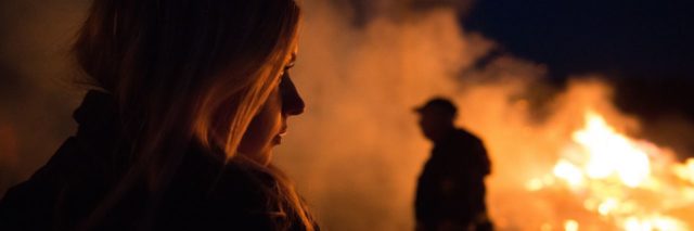 woman silhouetted and illuminated by flames looking at fire