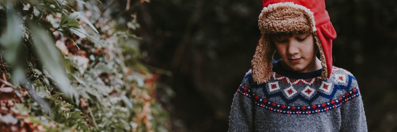 Childhood Signs of OCD Made Me Seem Like a 'Brat' young boy wearing sweater and hat walking through woods looking down