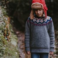 young boy wearing sweater and hat walking through woods looking down