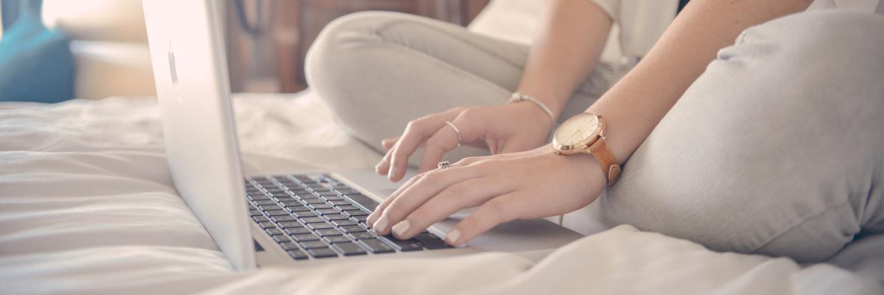 close up photo of woman sitting on bed with laptop and hands to keyboard to write