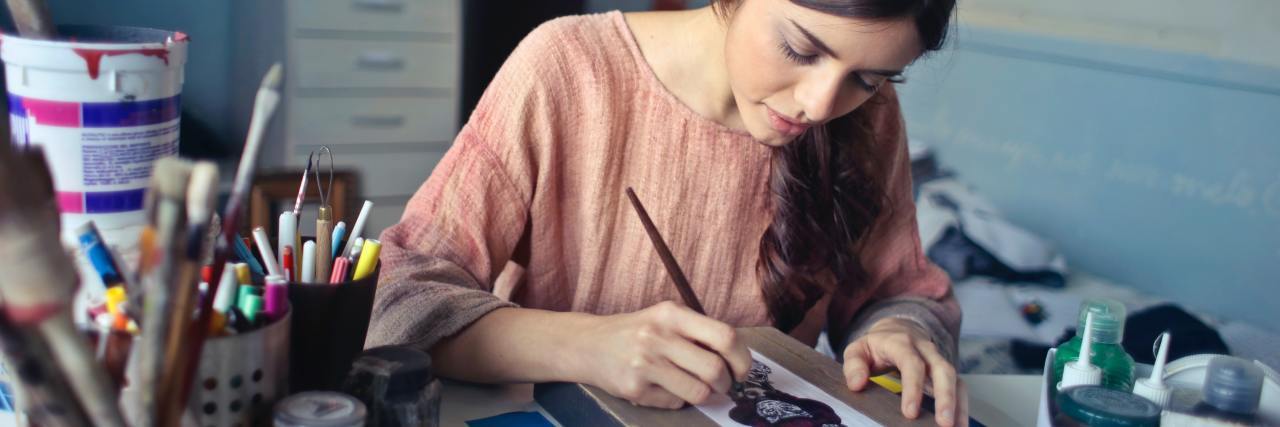 How to Make Your Own Mental Health Self-Care Kit woman designing box or painting on table surrounded by art supplies