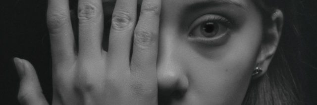 black and white close up image of young woman covering one eye with her hand and looking scared
