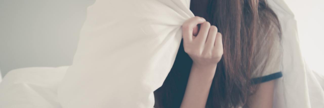 What a Day in Bed With Depression Is Really Like woman wrapped in blanket in bed with only hair and body showing