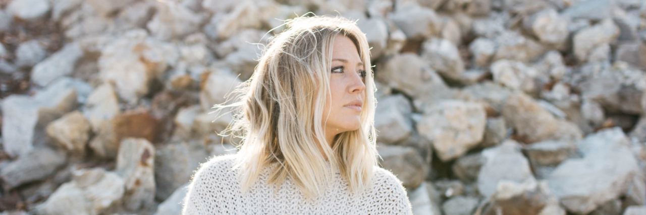 10 Ways I Combat Chronic Pain woman wearing a sweater and standing among rocks
