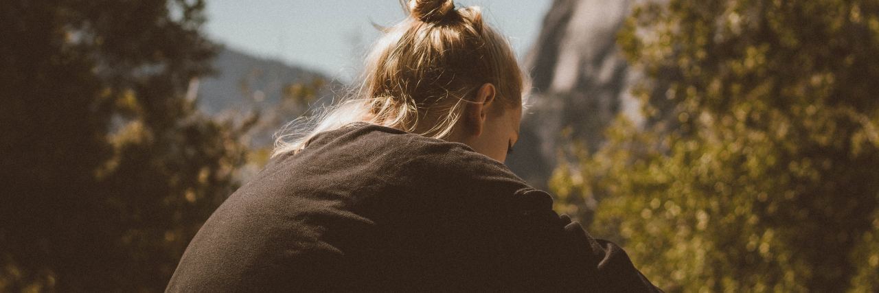 Why 'Tough Love' Doesn’t Work for Trauma Survivors woman sitting alone facing away in bright sunlight near trees and rocks
