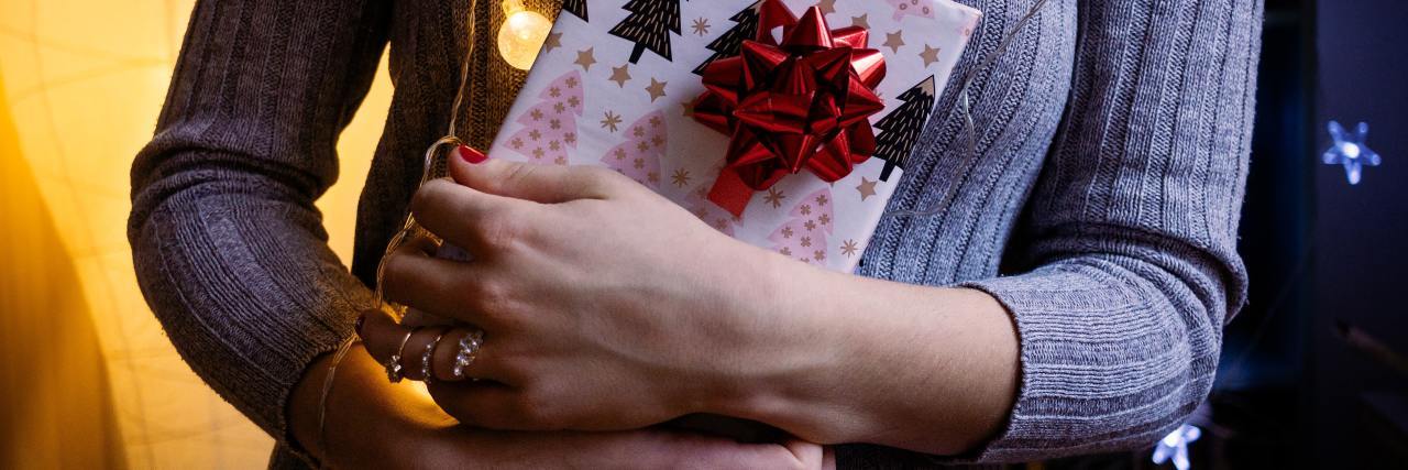 woman holding christmas gift with fairy lights around neck close up