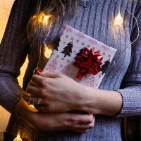 woman holding christmas gift with fairy lights around neck close up
