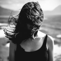 black and white photo of young woman standing on beach covering face with dark hair