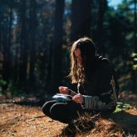 young woman sitting in woods writing with paper on knee
