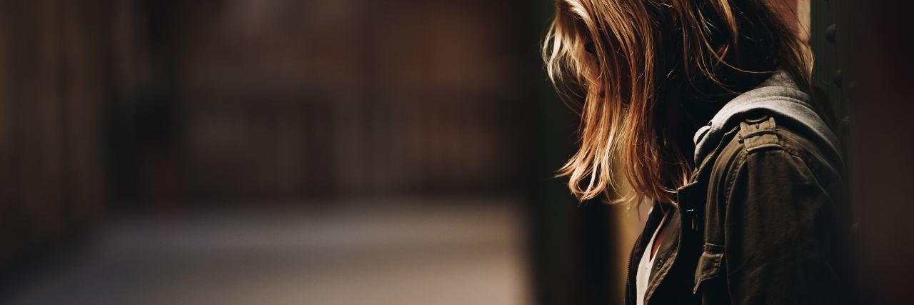 How to Cope With a Breakup When You Have Anxiety and Depression young woman with back to wall and hair covering face standing alone at night