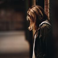 young woman with back to wall and hair covering face standing alone at night