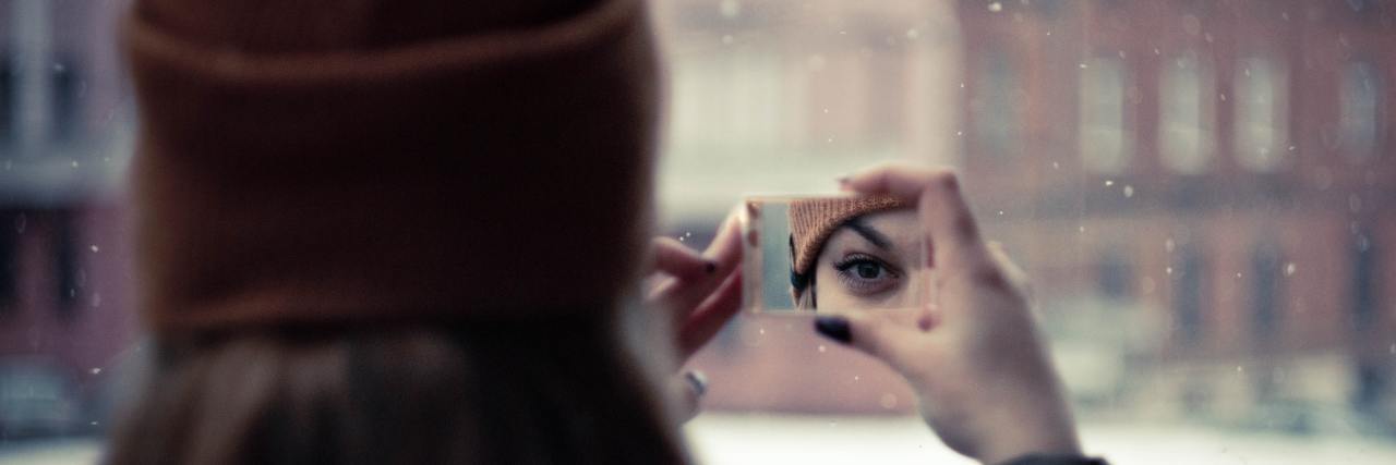 woman looking at reflection in mirror which shows only her eye