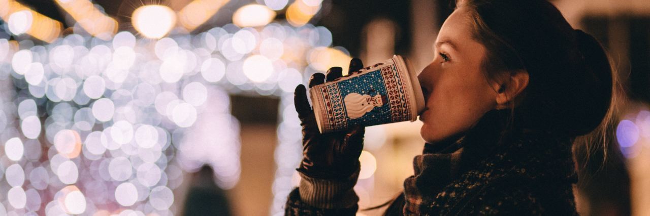young woman drinking takeaway coffee at christmas with blurred festive lights in background
