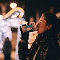 young woman drinking takeaway coffee at christmas with blurred festive lights in background