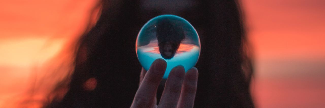 photo of woman framed against sunset holding crystal ball in front of face with inverted image refracted through ball