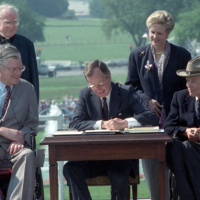 President Bush signs the Americans with Disabilities Act on the South Lawn of the White House. Sharing the dais with the President and he signs the Act are (standing left to right): Rev. Harold Wilkie of Clairmont, California; Sandra Parrino, National Council on Disability; (seated left to right): Evan Kemp, Chairman, Equal Opportunity Commission; and Justin Dart, Presidential Commission on Employment of People with Disabilities. Mrs. Bush and Vice President Quayle participate in the Ceremony. 26 July 1990 Photo credit: George Bush Presidential Library and Museum