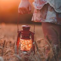 woman holding lamp in field of wheat at sunset