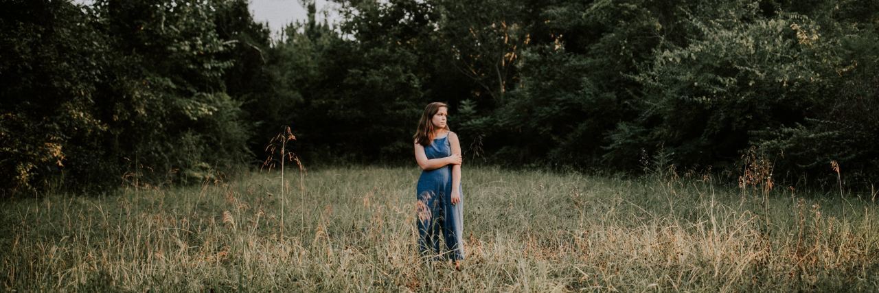 How to Be More Efficient With Chronic Illness young woman standing in field with trees behind her holding one arm