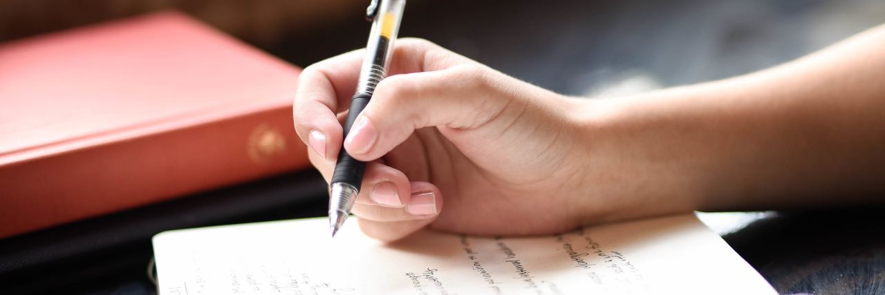 What to Know If You’re a Mental Health Writer or Artist close up of hand holding pen writing in notebook or journal