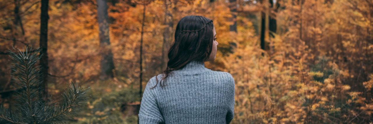 woman standing alone in fall woods facing away from camera