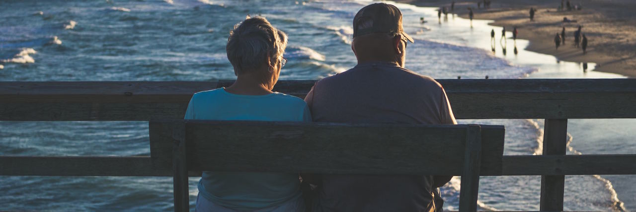 elderly couple sitting on bench looking at the ocean