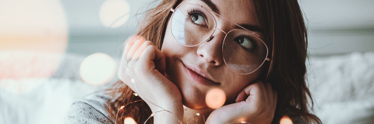 Why BPD Makes Me Daydream About a Perfect Fantasy World woman wrapped in fairy lights and daydreaming with chin resting on palms