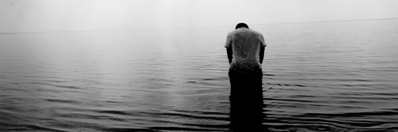black and white photo of man standing in shallow water hunched over symbol of depression