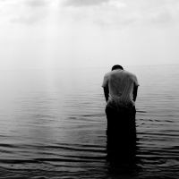 black and white photo of man standing in shallow water hunched over symbol of depression