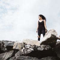 dark haired woman standing in strong pose on rocks and silhouetted by sky