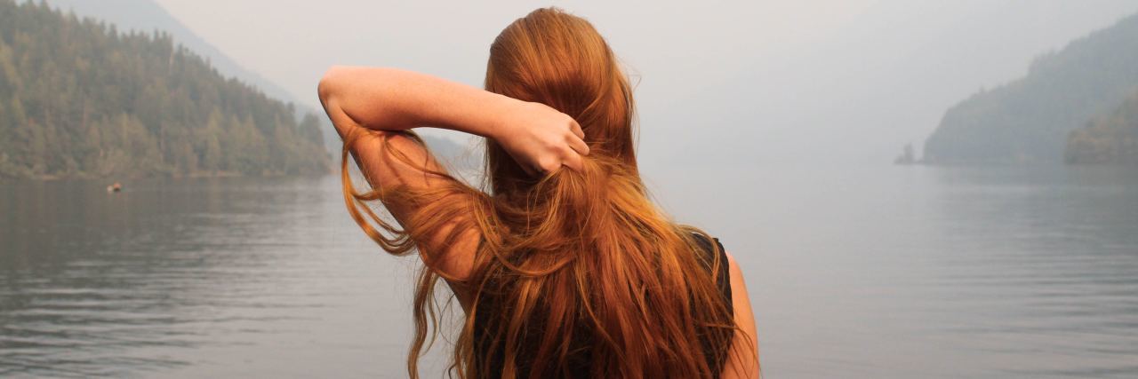 Dealing With Trauma After Life-Threatening Illness woman standing looking at lake in misty weather with hand in hair